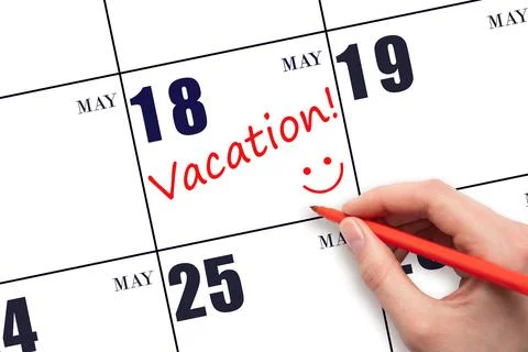 A hand writing a VACATION text and drawing a smiling face on a calendar date  Stock Photos