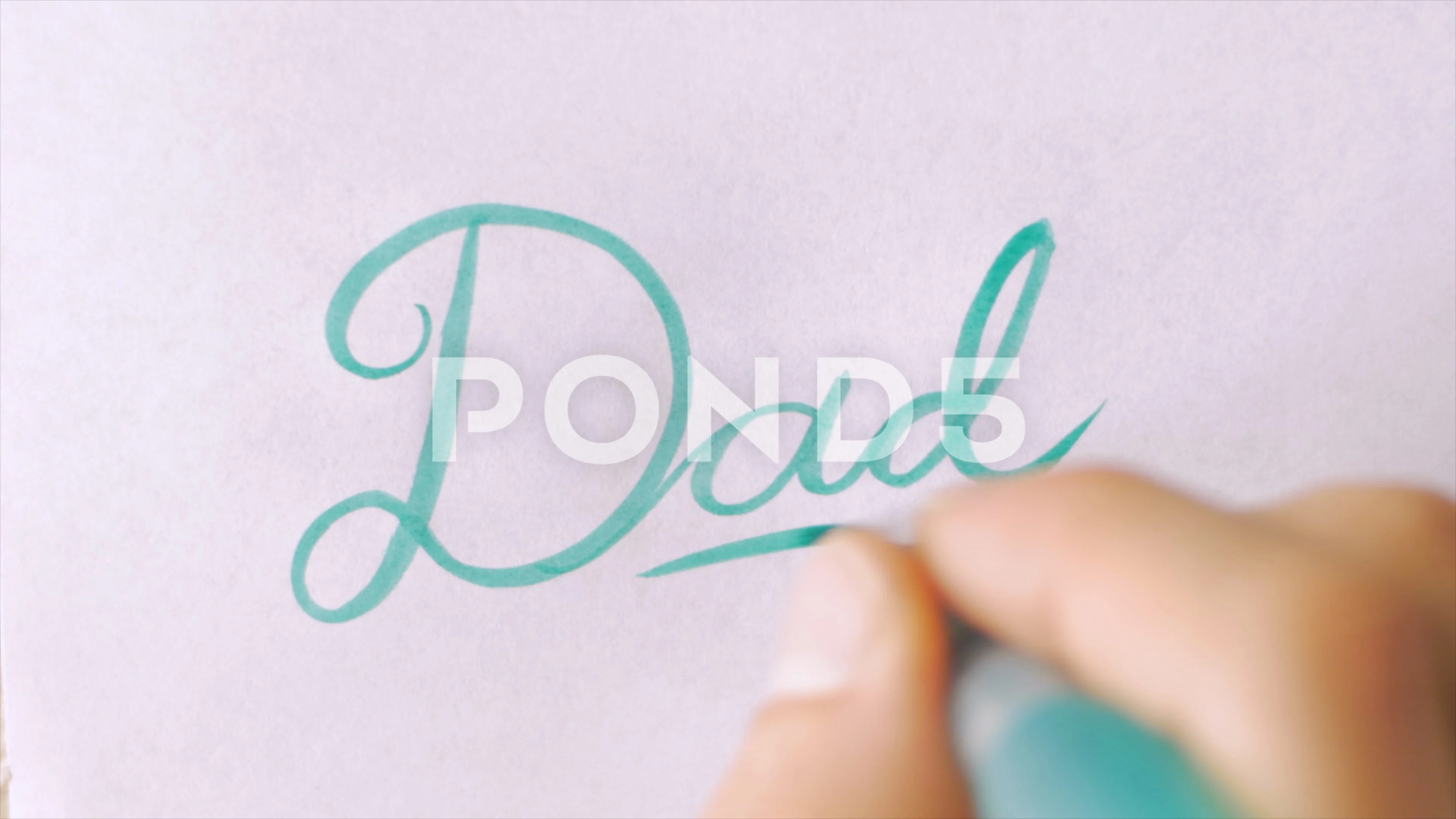 Hand writing the word DAD in cursive with a green brush pen