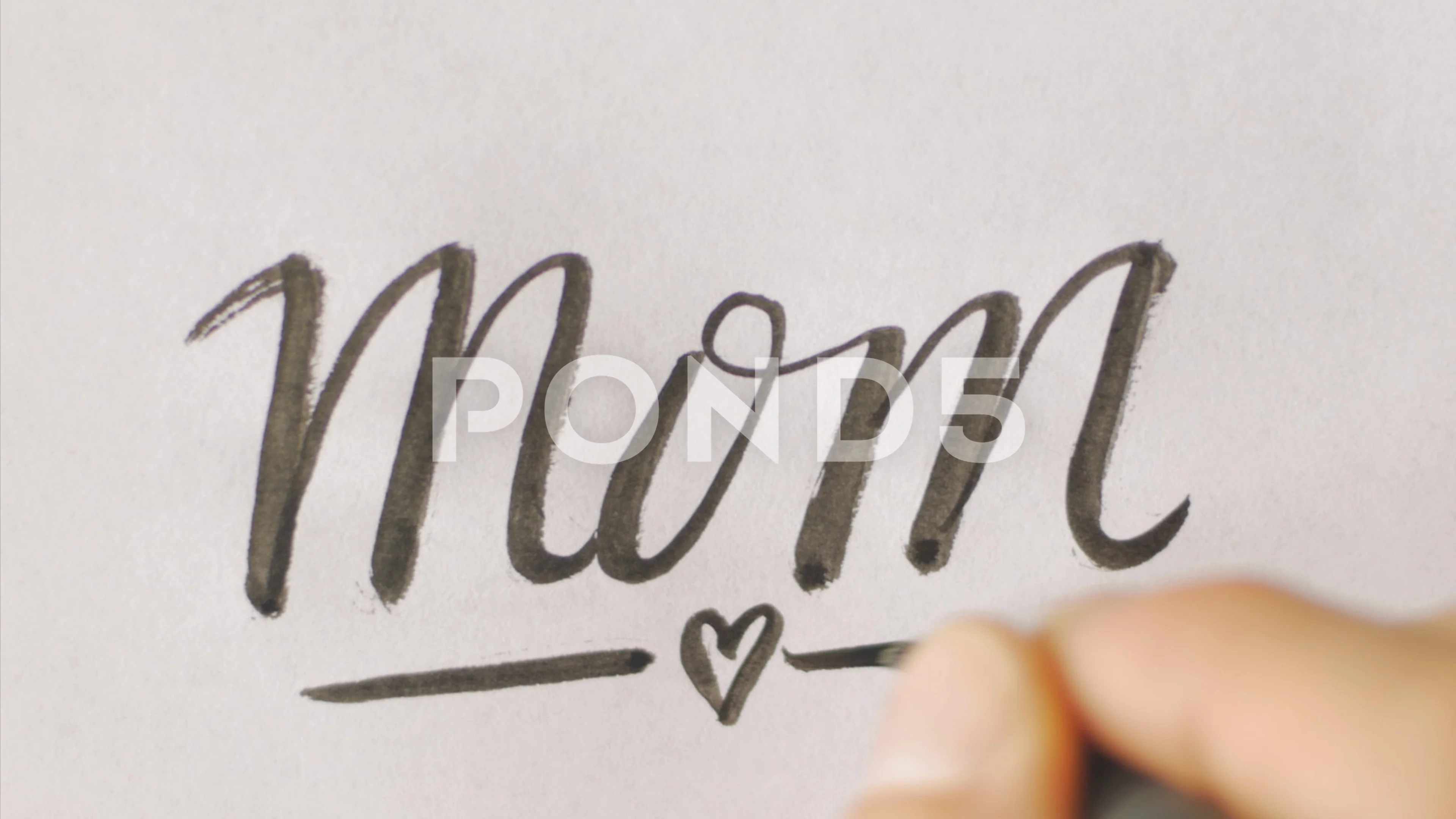 Hand writing the word MOM with a heart on white paper