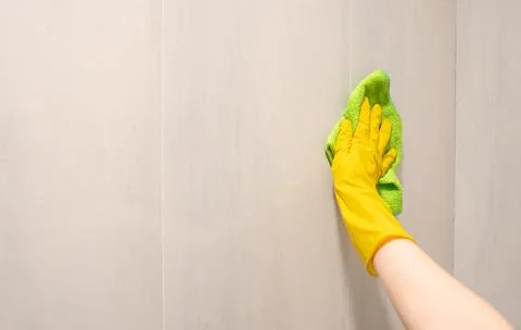 Hand in yellow rubber glove cleaning white tiled wall with green sponge in Stock Photos