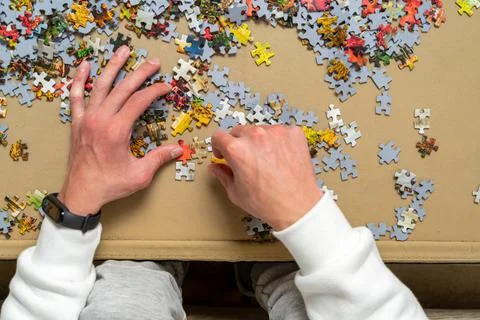 Hand of a young boy trying to solve a puzzle, he is putting together the smal Stock Photos