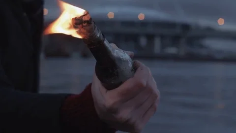 Hand of young man clutching burning Molotov cocktail bottle standing on coast Stock Footage