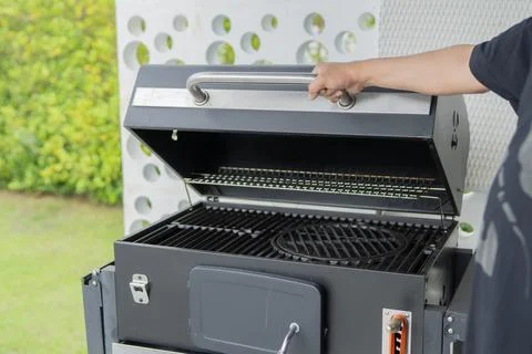 Hand of young man opening a backyard grill, charcoal BBQ grill and get read.. Stock Photos