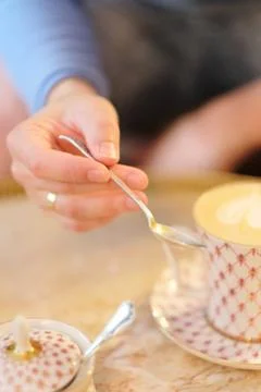 Hand of a young man with a spoon over a cup of coffee cappuccino on a table i Stock Photos