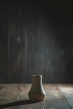 Handcrafted ceramic vase rests on a rustic wooden surface, illuminated by s.. Stock Photos