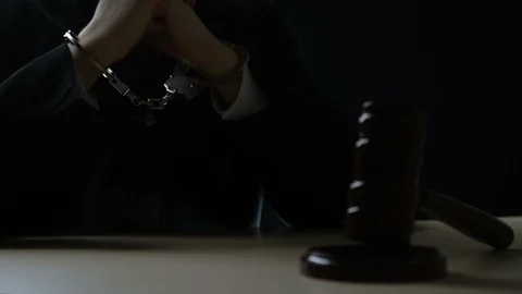 Handcuffed hands of corrupt judge sitting in dark courtroom, injustice, bribery Stock Footage 98049385