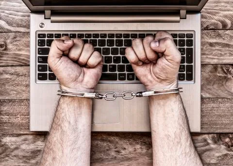 Handcuffed hands with laptop. Stock Photos