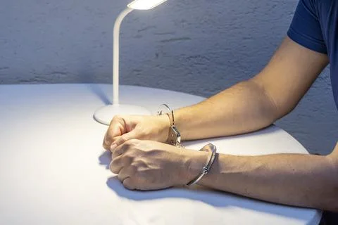 Handcuffed hands on table under lamp Foto stock