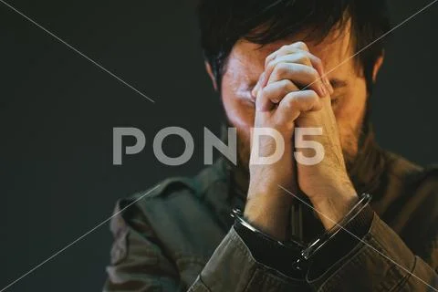 Handcuffed male prisoner in military uniform is praying Stock Photos
