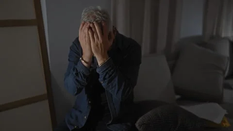 Handcuffed man covers his face in despair, sitting indoors with papers on a.. Stock-Footage 275436857