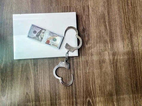 Handcuffs and money stack on a white envelope over wooden background Stock Photos
