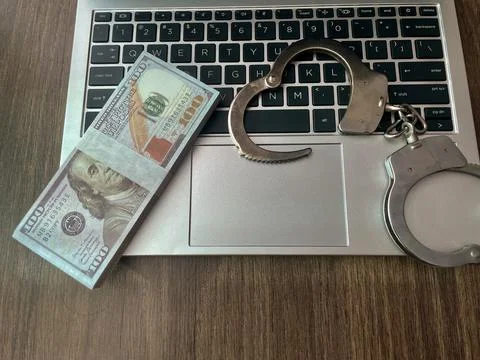 Handcuffs and a stack of money on a silver laptop keyboard Stock Photos