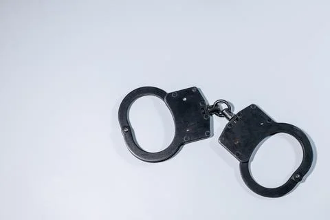 Handcuffs lying on a clean white surface, showcasing the metallic texture a.. Stock Photos