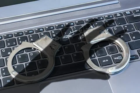 Handcuffs lying on a computer keyboard plus dark shadow (cybercrime) 写真素材