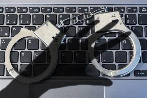 Handcuffs lying on computer keyboard plus dark shadow of a hand symbolizin... 写真素材