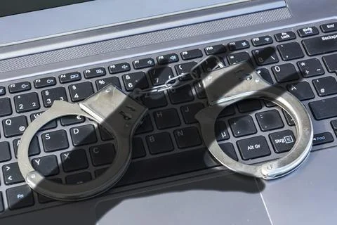 Handcuffs lying on a computer keyboard plus dark shadow of a hand symbolizing 写真素材