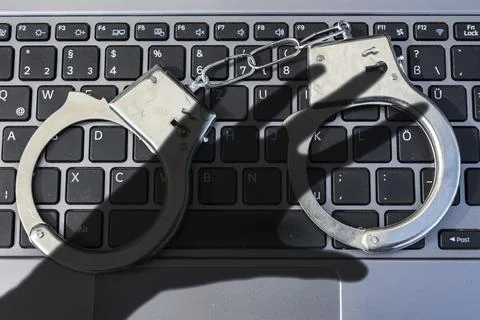 Handcuffs lying on computer keyboard plus dark shadow of a hand symbolizing 写真素材