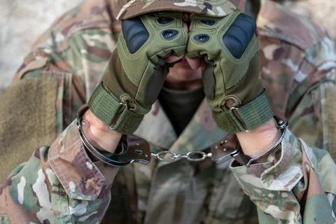 Handcuffs on raised hands of captive serviceman in close up 스톡 사진