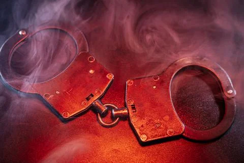 Handcuffs resting on a dark surface, surrounded by swirling smoke, creating.. Foto stock