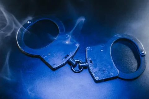 Handcuffs resting on a dark surface, surrounded by swirling smoke, creating.. Foto stock