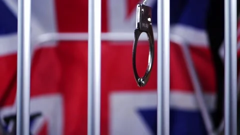 Handcuffs swing on prison bars with Union jack British flag background Stock Footage 182524635