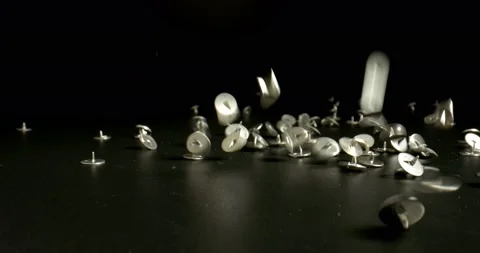 A handful of pushpins dropped on a black surface. Metal thumbtack, close up Stock Footage 146534503