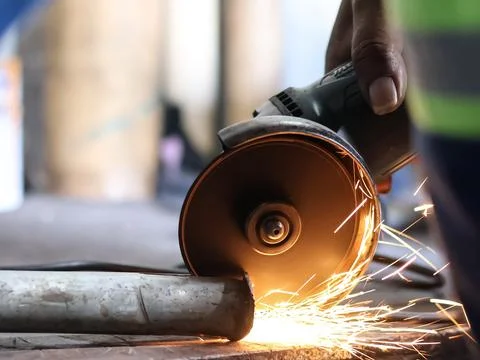 Handheld angle grinder cutting metal with sparks. Stock Photos