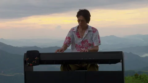 Handheld of Asian Man Playing Piano on Mountain Peak Sunset Landscape Stock Footage 340398982