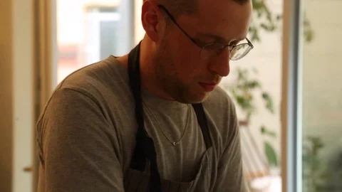 Handheld close-up shot of a man cooking while a woman walks in the kitchen Stock Footage 114846734