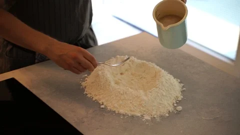 Handheld close-up shot of man pouring and mixing water in a flour hole Stock Footage 114884655