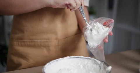 Handheld close-up shot, Woman's hands scooping whipped cream into a piping bag 스톡 동영상 308224165