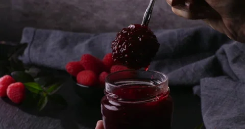 A handheld close-up of a spoon scooping thick raspberry jam from a jar. Fresh Stock Footage 298028838
