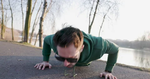 Handheld closeup of man doing push-ups in park during sunny afternoon Stock Footage 235681810