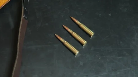 Handheld closeup of rounds of high caliber ammo, across to a large hunting rifle Stock Footage 64092457