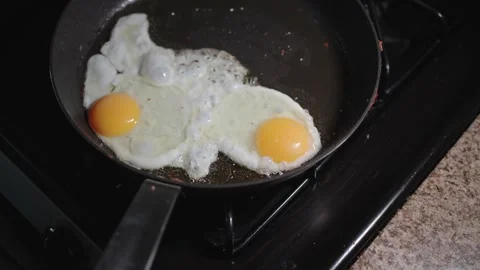 Handheld footage of two fried eggs sizzling in a pan on a stovetop Stock Footage 314291824