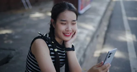 Handheld high angle view shot, Cheerful Asian woman sits on an outdoor side.. Vidéo 299779494