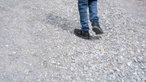Handheld Low Angle Tracking Shot of Man in Jeans and Sneakers Walking on Path Stock Footage 332684767