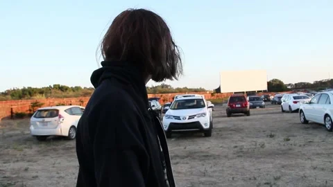 Handheld pan around sad looking teen at drive in theatre Stock Footage 150448362