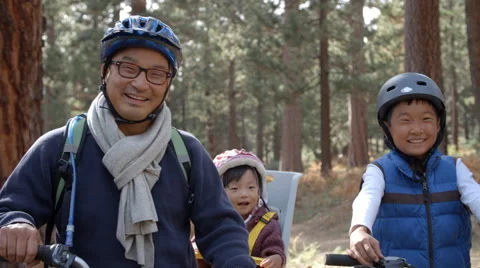 Handheld pan of Asian family on bikes in a forest, close up Stock Footage