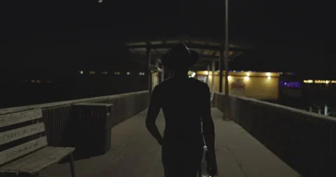 Handheld rear view shot of man holding gig bag and walking on bridge at night 스톡 동영상 147102235