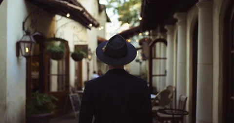 Handheld rear view of young man with hat standing in alley with restaurants 스톡 동영상 146959511