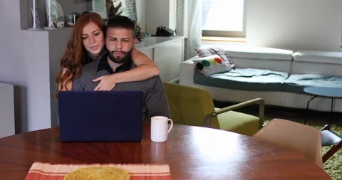 Handheld shot of affectionate young couple talking and using laptop at home Stock Footage 119889224