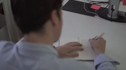 Handheld shot and rack focus of young man writing in notebook Stock Footage 114878100