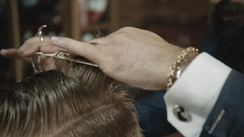 Handheld shot of barber combing and cutting a man's hair with scissors in a Video stock 117702627