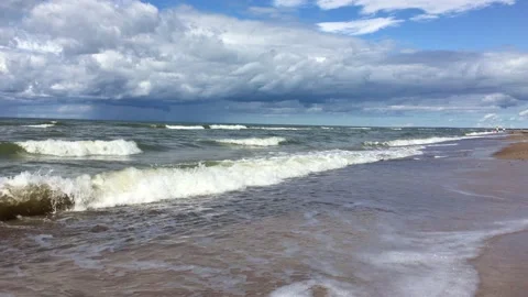 A handheld shot of beach with sand and waves crushing stone with seaweed Stock Footage 198531274