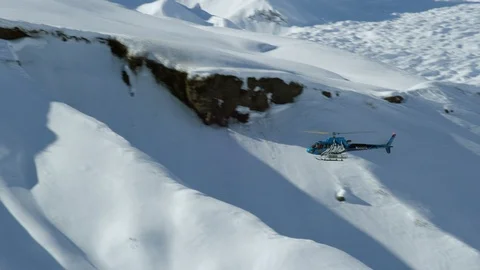 Handheld shot of blue helicopter flying above rocky mountains covered in snow Stock Footage 129128192