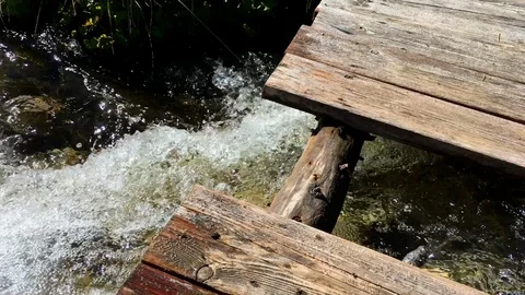Handheld shot of clear water in stream flowing below wooden footbridge Stock Footage 120426318