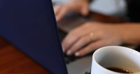 Handheld shot of coffee mug besides laptop and young woman working on it Stock Footage 119936568