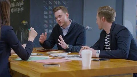 Handheld shot of colleagues discussing while sitting at table in creative office Stock Footage