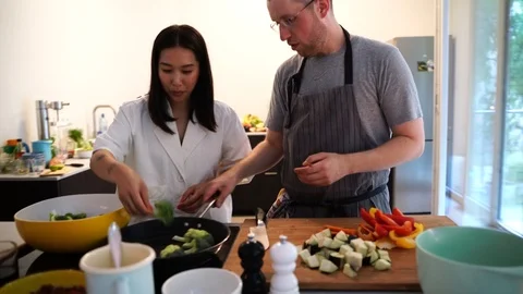 Handheld shot of couple adding broccoli into frying pan in kitchen Stock Footage 114883420